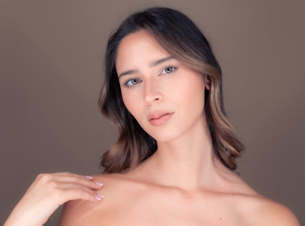 Close-up portrait of a young woman with brown hair against a soft brown background.